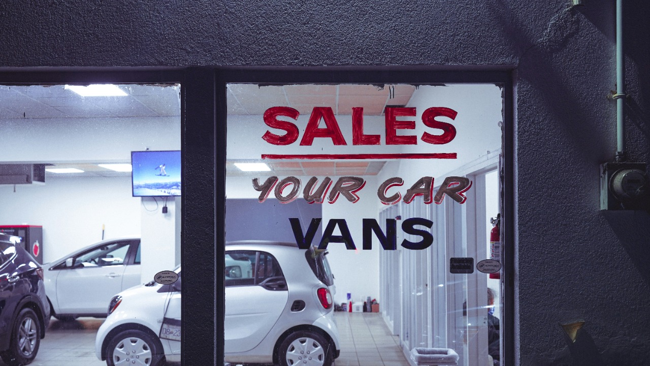Image Credit: a car dealership with a sales sign in the window — Chelaxy Designs