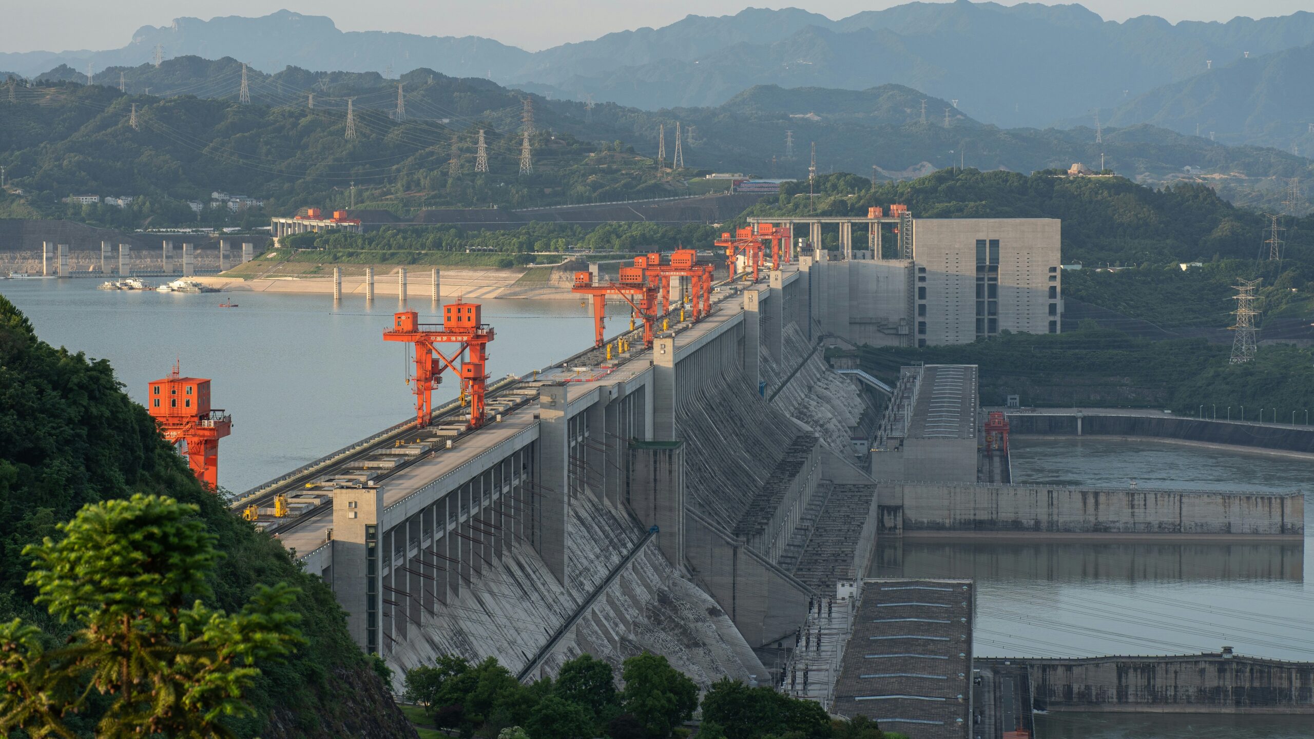 Massive hydroelectric dam with red structures against a mountain backdrop. Massive hydroelectric dam with red structures against a mountain backdrop.