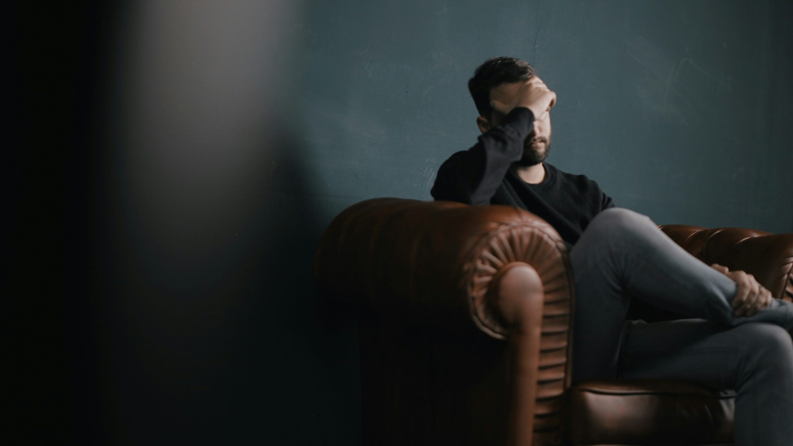 a man holds his head while sitting on a sofa a man holds his head while sitting on a sofa